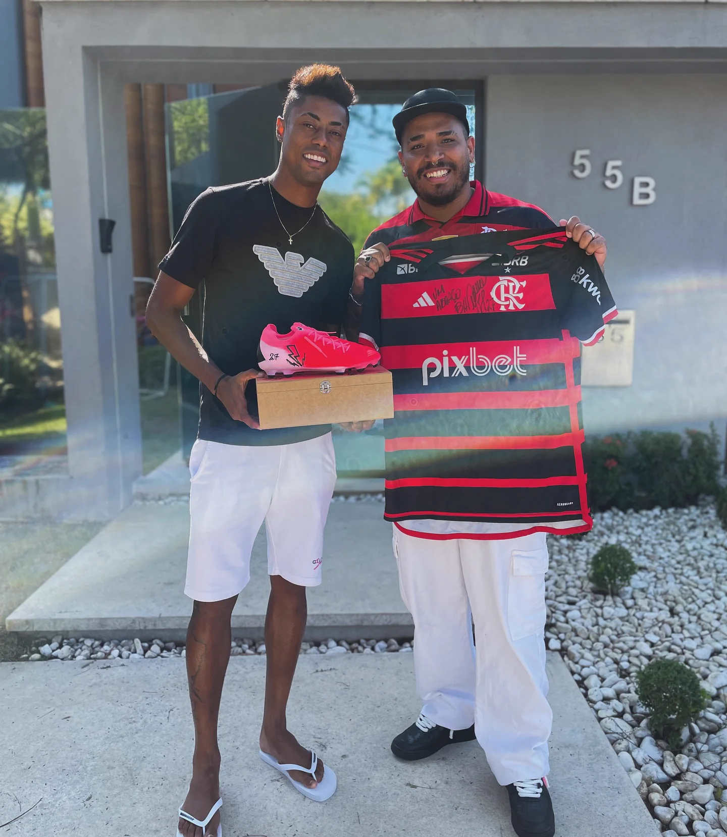 Bruno Henrique segurando uma chuteira rosa pintada à mão ao lado de Gabriel Freire com a camisa do Flamengo