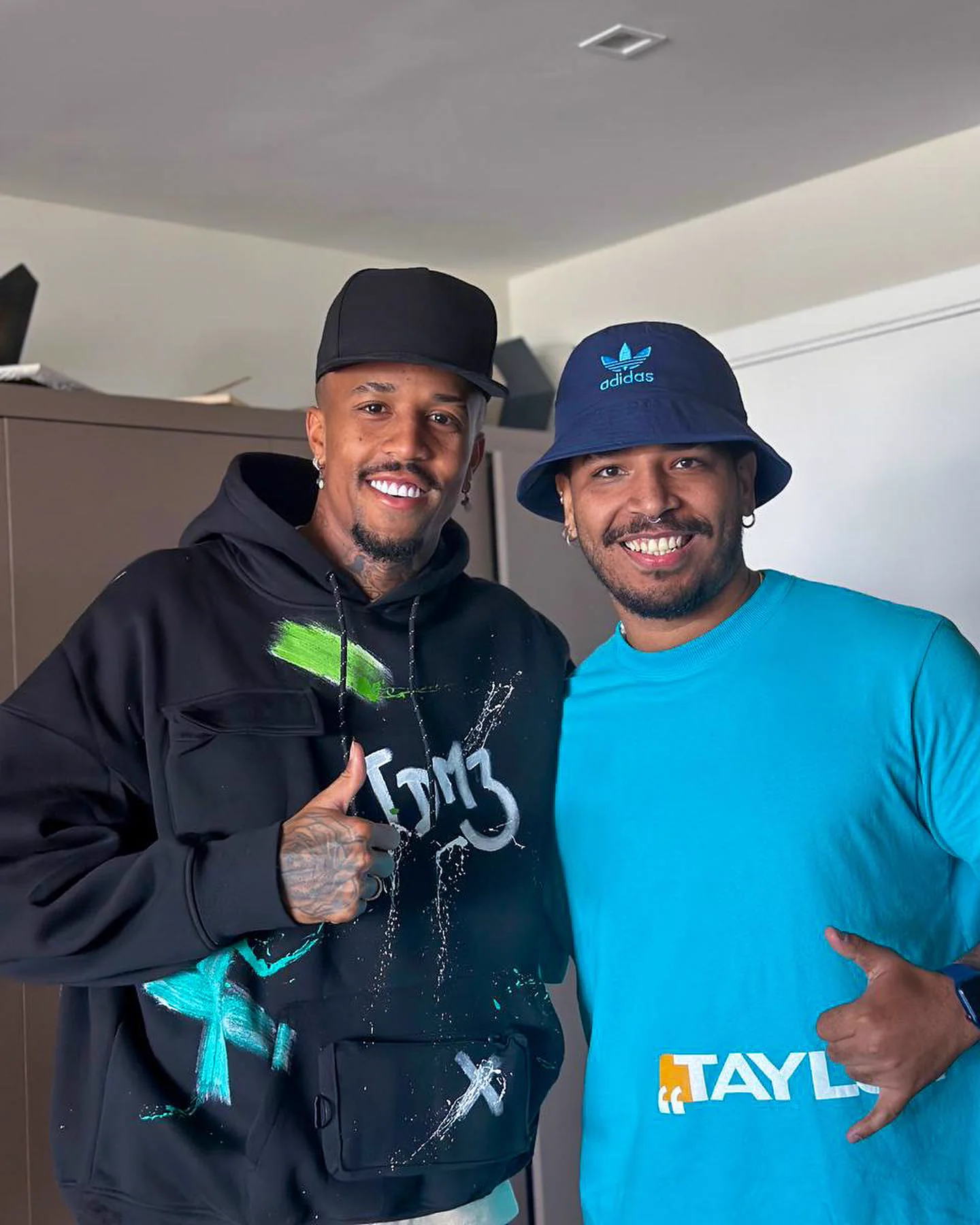 Éder Militão vestindo um moletom preto pintado à mão, ao lado de Gabriel Freire