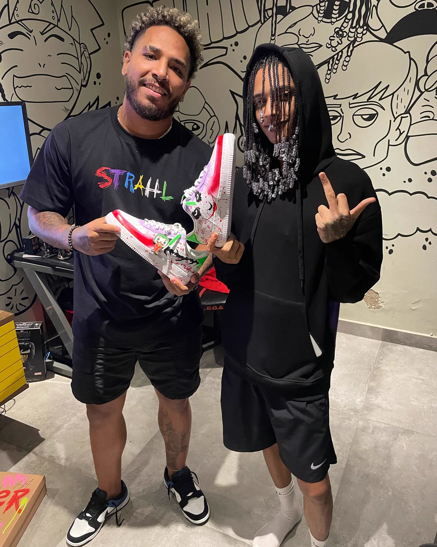 Gabriel Freire ao lado de Oruam segurando um par de Air Force 1 pintado com o Coringa