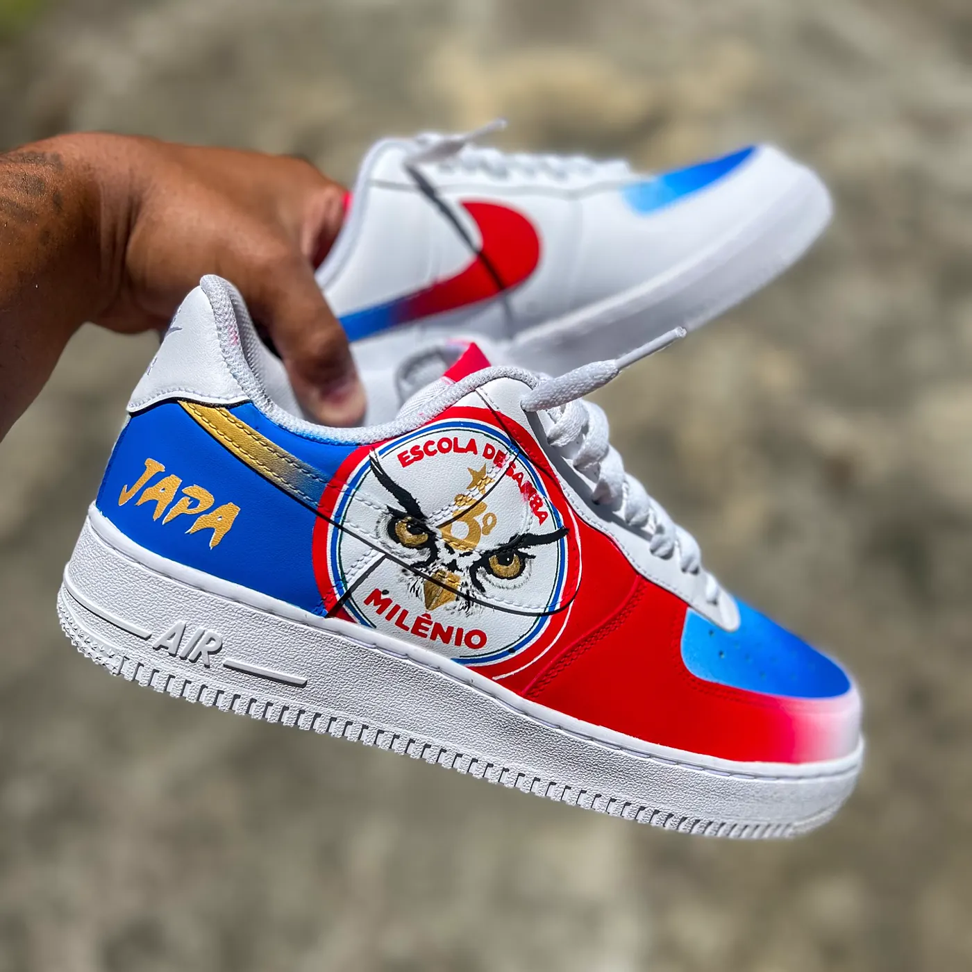 Par de Air Force 1 em vermelho, azul e branco com a coruja da Escola de Samba Milênio e o nome Japa em dourado