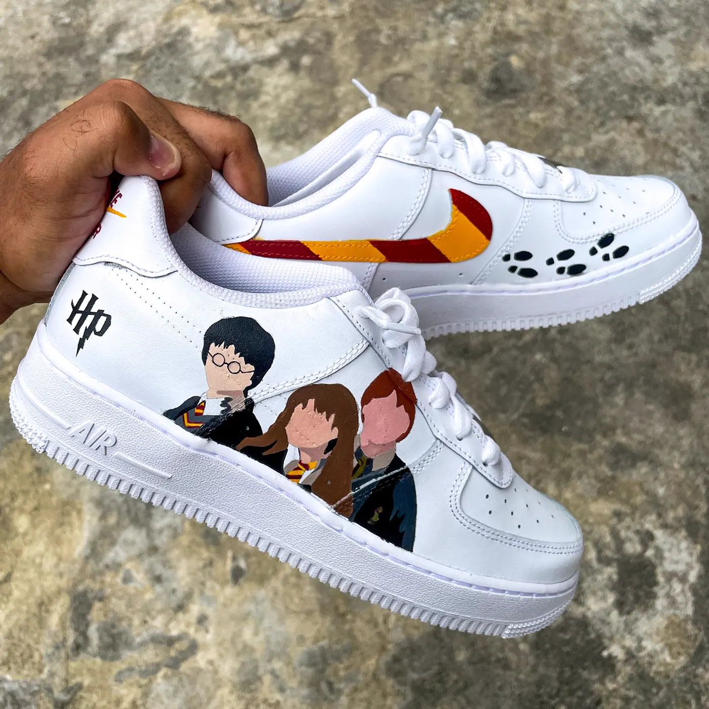 Par de Air Force 1 branco com Harry, Hermione e Rony, swoosh nas cores da Grifinória e pegadas do Mapa do Maroto