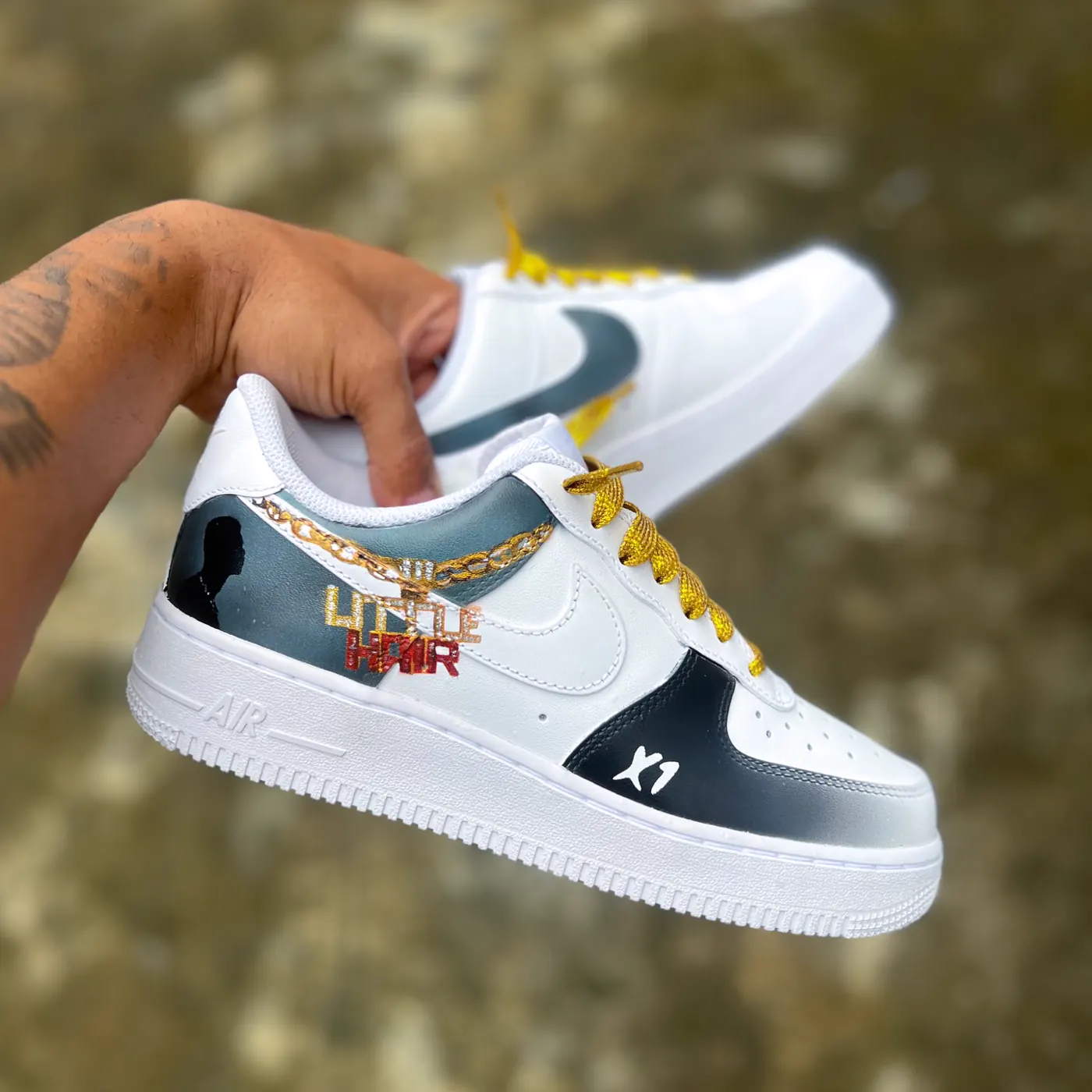Par de Air Force 1 branco e preto com corrente dourada pintada, cadarço dourado e a inscrição Little Hair